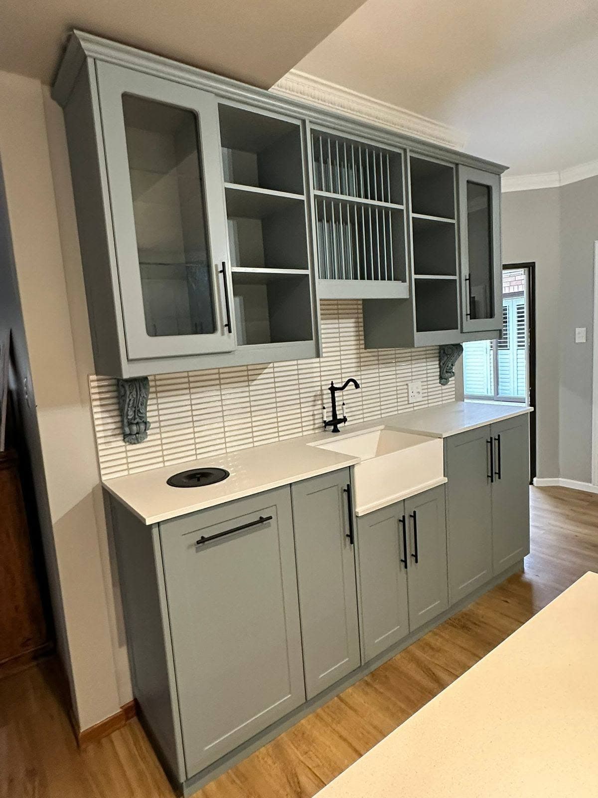 Fitted grey display cabinets around a white farmhouse sink